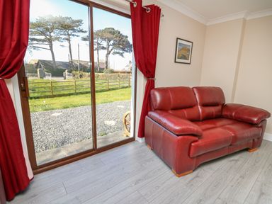 A red leather sofa next to sliding glass doors with red curtains in a room at Glyn Cottage in Llanon