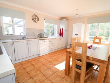 A kitchen with white cabinets a wooden dining table and chairs a white refrigerator and microwave at Glyn Cottage in Llanon