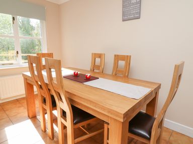 A dining room with a wooden table and six wooden chairs with dark seats at Glyn Cottage in Llanon