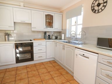 A kitchen with white cabinets, a double oven, dish rack, microwave, and tiled floor at Glyn Cottage in Llanon