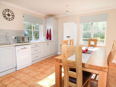 A kitchen with wooden dining table and chairs white cabinets dishwasher microwave and windows at Glyn Cottage in Llanon