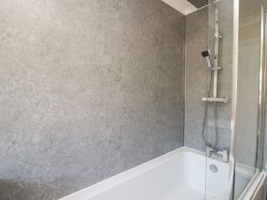 A bathroom with a bathtub and a shower area with a glass screen at Glyn Cottage in Llanon