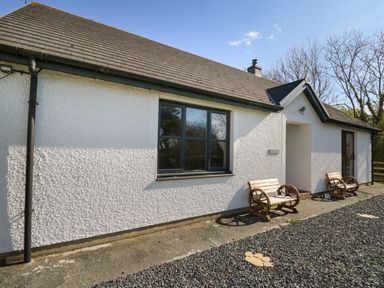 Exterior view of a white cottage with two wooden benches and gravel in front at Glyn Cottage in Llanon