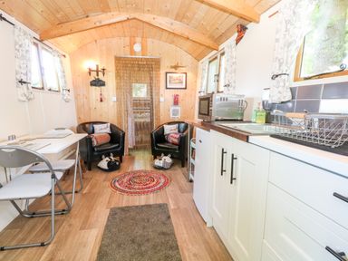 A small kitchen and sitting area with two black chairs a white table with chairs a microwave and sink at Hugatree in Little Dunham near Litcham