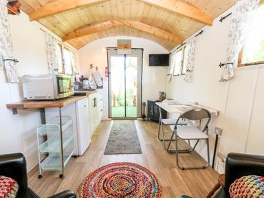 A narrow room with a wooden ceiling a kitchen counter with a microwave a small dining table with two chairs and a wall-mounted TV at Hugatree in Little Dunham near Litcham