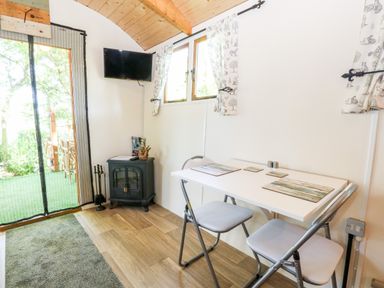 A small dining area with a white table and two folding chairs near windows and a wall mounted television at Hugatree in Little Dunham near Litcham