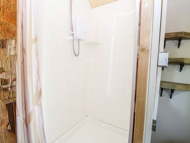 A shower area with a white electric shower unit and a shower curtain in a bathroom at Hugatree in Little Dunham near Litcham
