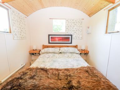 A bedroom with a bed with patterned bedding a fur throw two windows wood ceiling and a wall picture at Hugatree in Little Dunham near Litcham