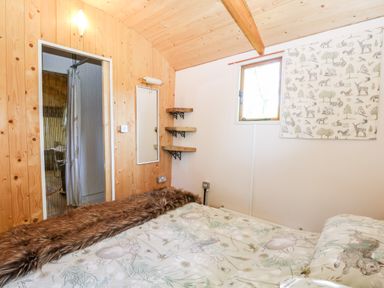 A bedroom with wood paneled walls bed with animal print bedding small window and wooden corner shelves at Hugatree Little Dunham near Litcham