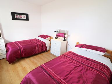 A bedroom with two single beds with red bed linens and a white chest of drawers with a mirror and lamps between them at Ard an Phiobaire in An Luinnigh near Derrybeg County Donegal