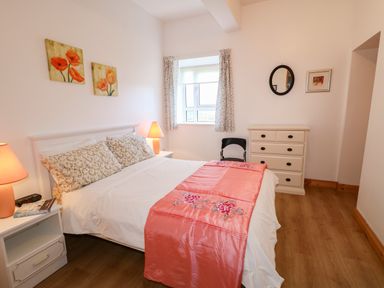 A bedroom with a double bed next to a window a white chest of drawers and bedside tables with lamps at Ard an Phiobaire in An Luinnigh near Derrybeg County Donegal