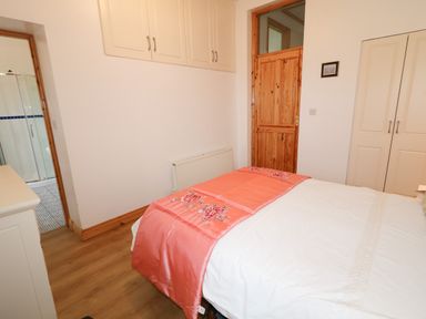 A bedroom with a bed covered in white and coral bedding a wooden door built in wardrobes and a view of a bathroom at Ard an Phiobaire in An Luinnigh near Derrybeg County Donegal