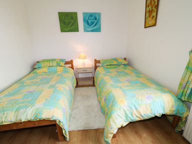 A bedroom with two single beds with floral bedspreads a nightstand with a lamp between the beds and flower paintings on the walls at Ard an Phiobaire in An Luinnigh near Derrybeg County Donegal