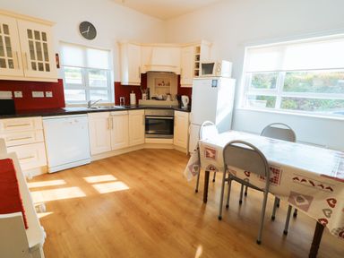 A kitchen with white cabinets a dishwasher a stove a refrigerator a microwave and a dining table with chairs at Ard an Phiobaire in An Luinnigh near Derrybeg County Donegal