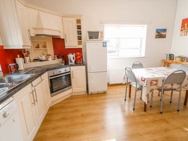 A kitchen with white cabinets a refrigerator a stove a table with chairs and a window at Ard an Phiobaire An Luinnigh near Derrybeg County Donegal