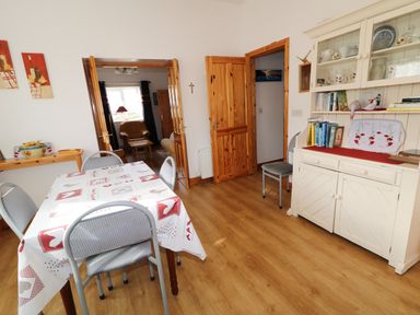 A dining room with a table and chairs a white cabinet with books and dishes and wooden doors at Ard an Phiobaire in An Luinnigh near Derrybeg County Donegal