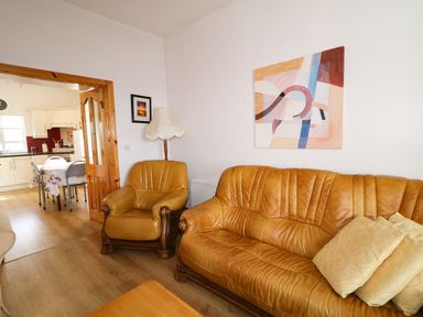 A living room with a leather sofa and armchair next to a lamp and an abstract painting on the wall at Ard an Phiobaire in An Luinnigh near Derrybeg County Donegal