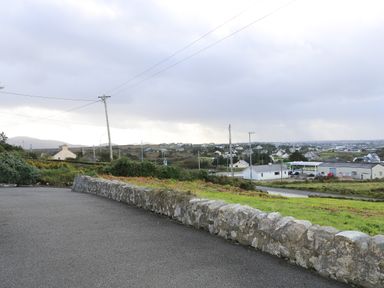 A road with stone wall and houses in the distance at Ard an Phiobaire in An Luinnigh near Derrybeg County Donegal