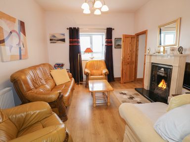 A living room with leather sofas a wooden coffee table a fireplace with a fire a window with curtains and a standing lamp at Ard an Phiobaire in An Luinnigh near Derrybeg County Donegal
