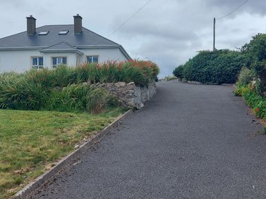 A driveway with hedges and grasses leading to a white house with a dark roof and chimneys at Ard an Phiobaire in An Luinnigh near Derrybeg County Donegal