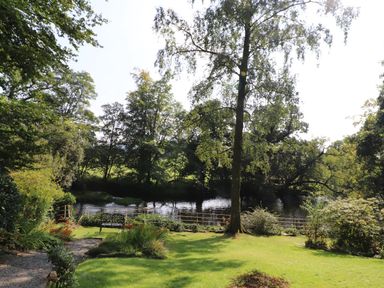 A garden with a bench overlooking a river surrounded by trees at The Old Carriage House in Clappersgate