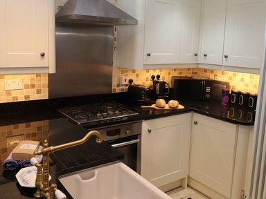 A kitchen with white cabinets black countertops and a brass faucet at The Old Carriage House in Clappersgate