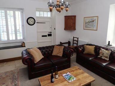 A sitting room with two leather sofas a wooden coffee table clock on the wall and a wooden cabinet at The Old Carriage House in Clappersgate