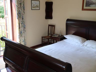 A bedroom with a wooden bed white bedding a wooden chair and a bedside table with a bottle and a magazine at The Old Carriage House in Clappersgate