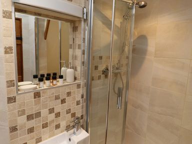 A bathroom with a shower enclosure a small sink and toiletries on a tiled shelf at The Old Carriage House in Clappersgate