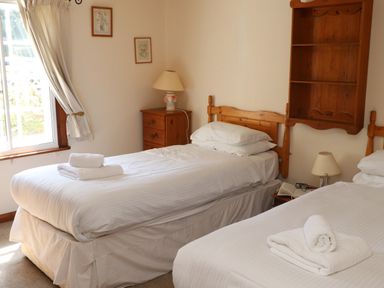A bedroom with two single beds white linens towels a wooden bedside table with a lamp and window with curtains at The Old Carriage House in Clappersgate