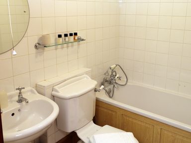 A bathroom with a sink toilet bathtub and toiletries on a glass shelf at The Old Carriage House in Clappersgate