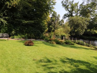 A garden with a green lawn a bench and trees near a river at The Old Carriage House in Clappersgate