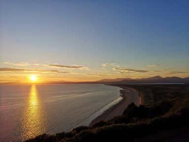 A sunset over a curved coastline with mountains in the distance at Y Bwthyn in Llanbedr