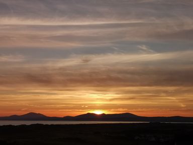 A sunset over mountains with a body of water and a dark land silhouette at Y Bwthyn in Llanbedr