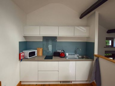 A kitchen area with white cabinets a microwave a red kettle a toaster a sink and a dish rack at Old Sawrey Stores in Hawkshead