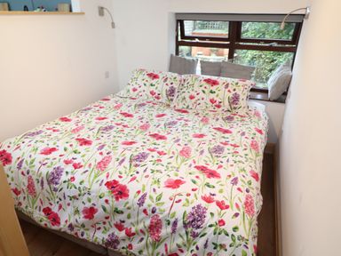 A bedroom with a bed with floral bedding and pillows by a window with cushions at Old Sawrey Stores Hawskhead