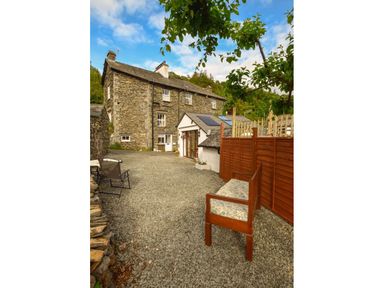 An outdoor gravel area with seating and a stone house in the background at Old Sawrey Stores in Hawskhead