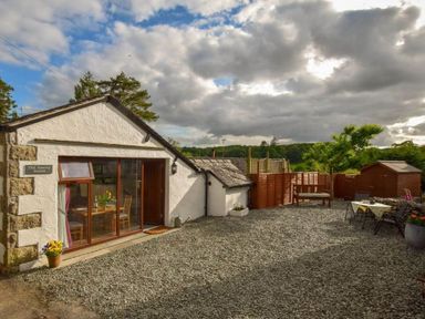 A gravel courtyard with outdoor seating and a small wooden shed beside a white building at Old Sawrey Stores in Hawskhead