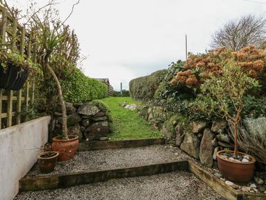 A garden path with gravel steps and potted plants bordered by stone walls and hedges at Kernyk in Perranuthnoe