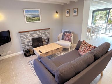 A living room with a gray sofa, armchair, coffee table, fireplace, and wall art at Kernyk in Perranuthnoe
