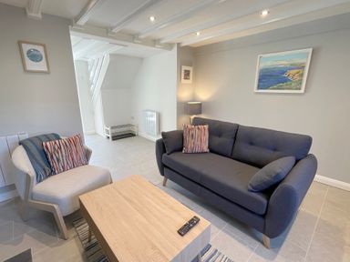 A living room with a dark sofa and light armchair with striped cushions and a wooden coffee table at Kernyk in Perranuthnoe