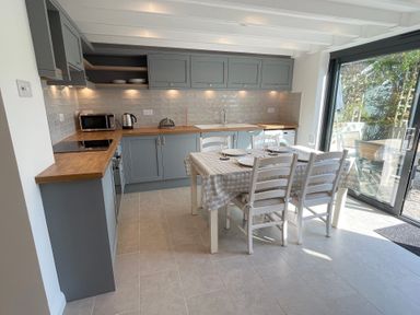 A kitchen with gray cabinets wooden countertops a dining table set for four near a sliding glass door at Kernyk in Perranuthnoe