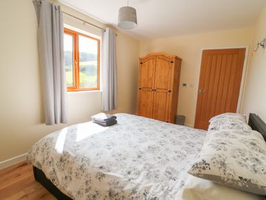 A bedroom with a double bed a wardrobe a wooden door and a window with curtains at Ploony Hill Cabin in Bleddfa near Knighton
