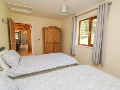 A bedroom with two beds a wooden wardrobe and a window with curtains at Ploony Hill Cabin in Bleddfa near Knighton