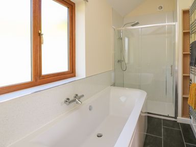 A bathroom with a bathtub under a window and a glass enclosed shower at Ploony Hill Cabin Bleddfa near Knighton