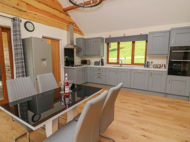 A kitchen with grey cabinets a black dining table with chairs and a bottle with glasses at Ploony Hill Cabin in Bleddfa near Knighton