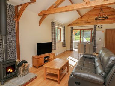 A living room with a leather couch wooden coffee table TV wood stove and dining table at Ploony Hill Cabin in Bleddfa near Knighton