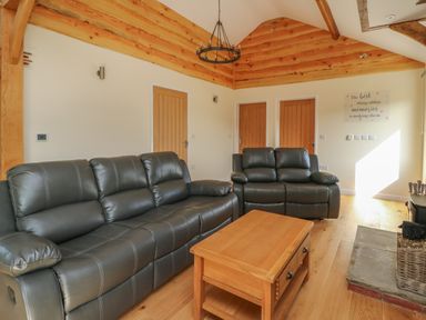 A living room with two leather sofas a wooden coffee table wooden doors and a sign on the wall at Ploony Hill Cabin in Bleddfa near Knighton