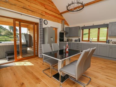 A kitchen with grey cabinets a dining table with four chairs and a sliding glass door leading outside at Ploony Hill Cabin in Bleddfa near Knighton