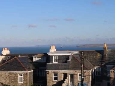 Rooftops of houses with chimneys and a view of the sea and distant coastline at The Beach Hut in St Ives